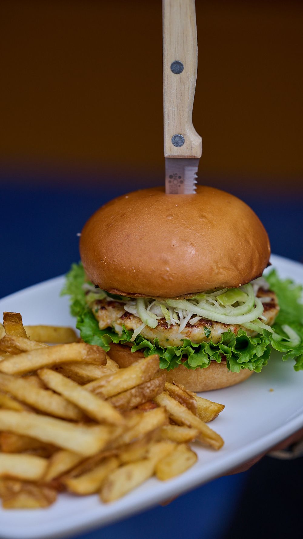 A juicy hamburger with lettuce and onions served alongside golden french fries on a white plate.