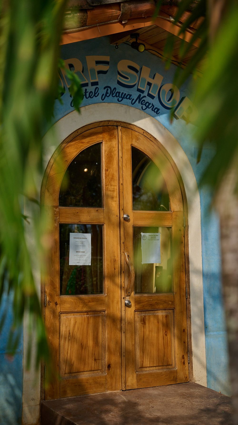 A series of three wooden arched doorways with blue signage photographed in soft natural lighting through leaves.