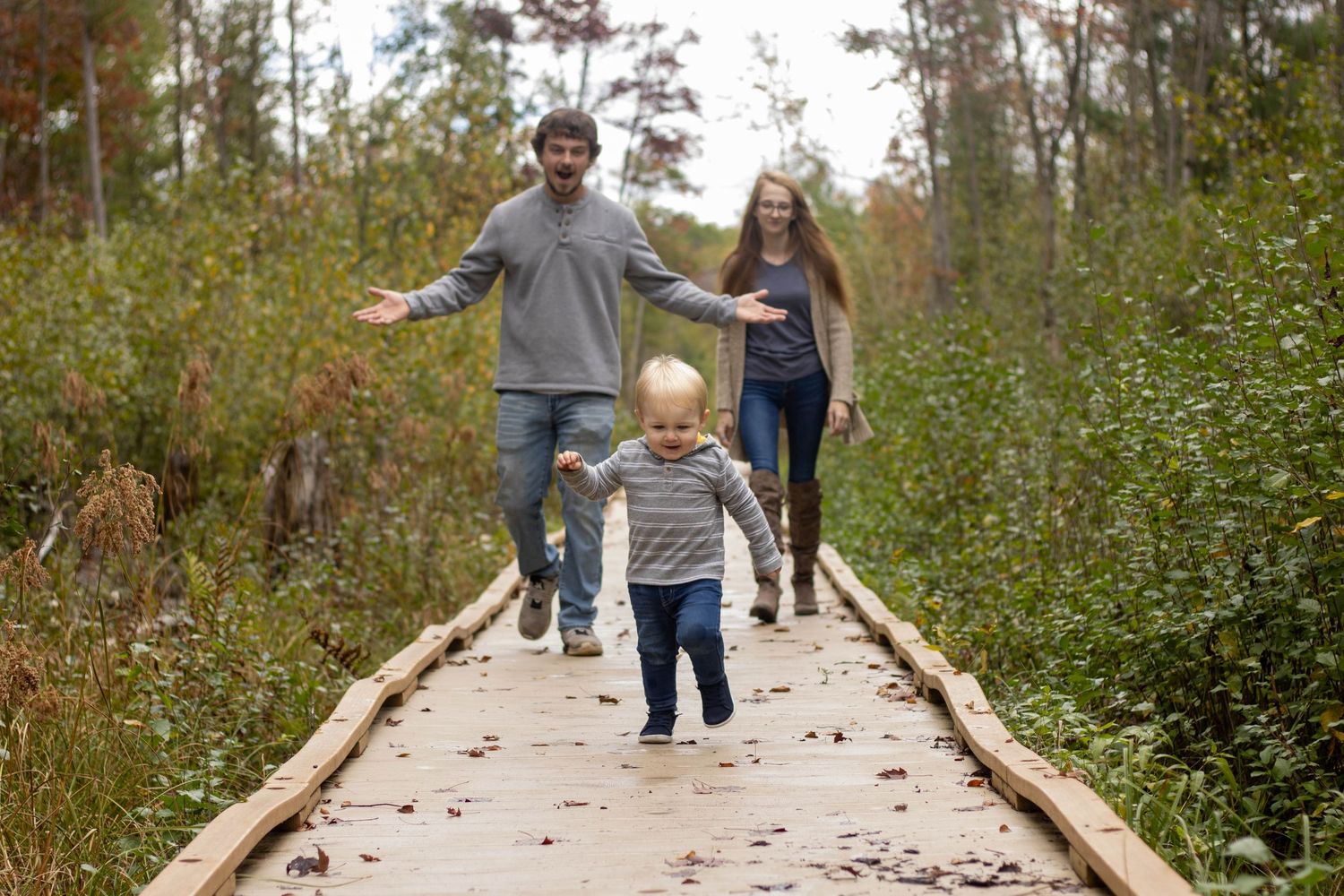 Family walking together on a wooden boardwalk path through lush green nature during autumn season.