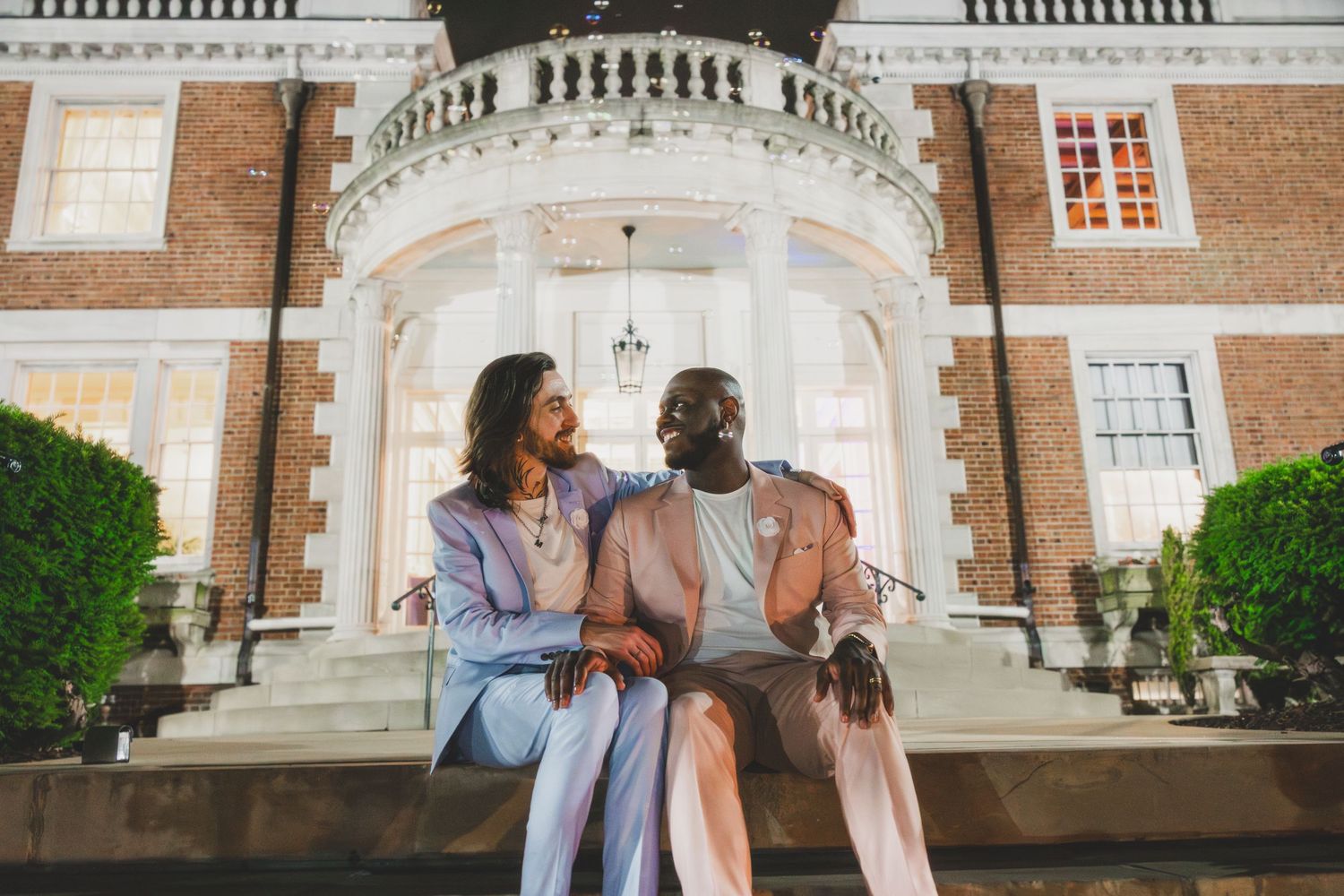 A couple sits and chats on grand stone steps of a historic brick building.
