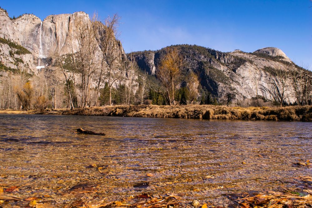 Snow-capped granite cliffs reflect in clear waters of Merced River in Yosemite Valley.