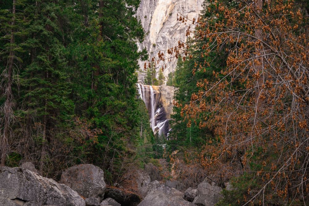 A cascading waterfall flows down granite cliffs surrounded by evergreen trees and autumn foliage.