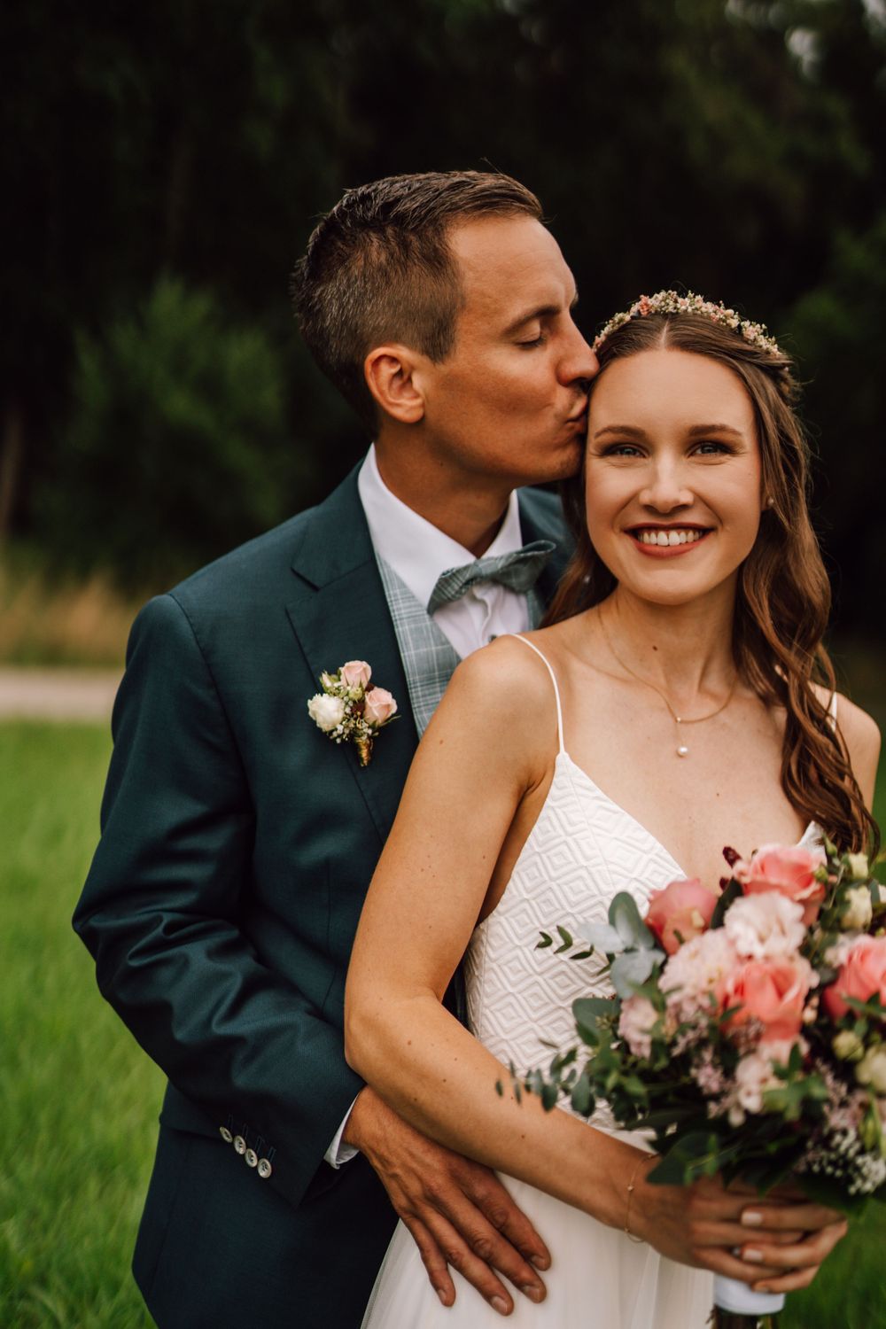 Wedding couple embraces tenderly in a garden setting with pink floral bouquet.