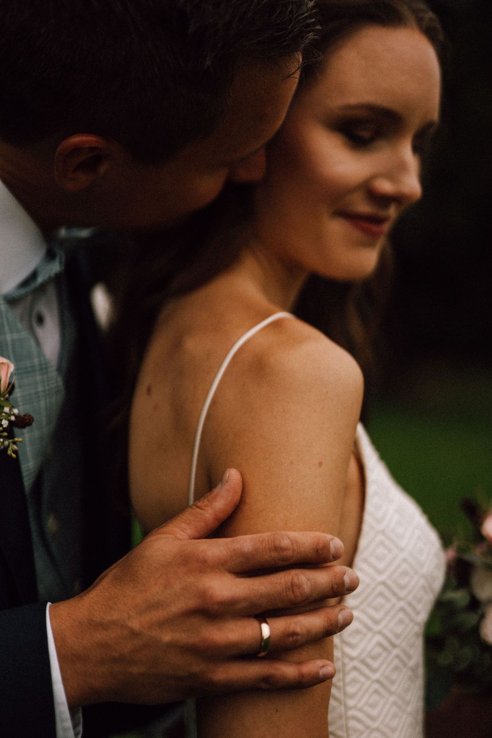 Close-up detail shot of hands and lace wedding dress in moody lighting.