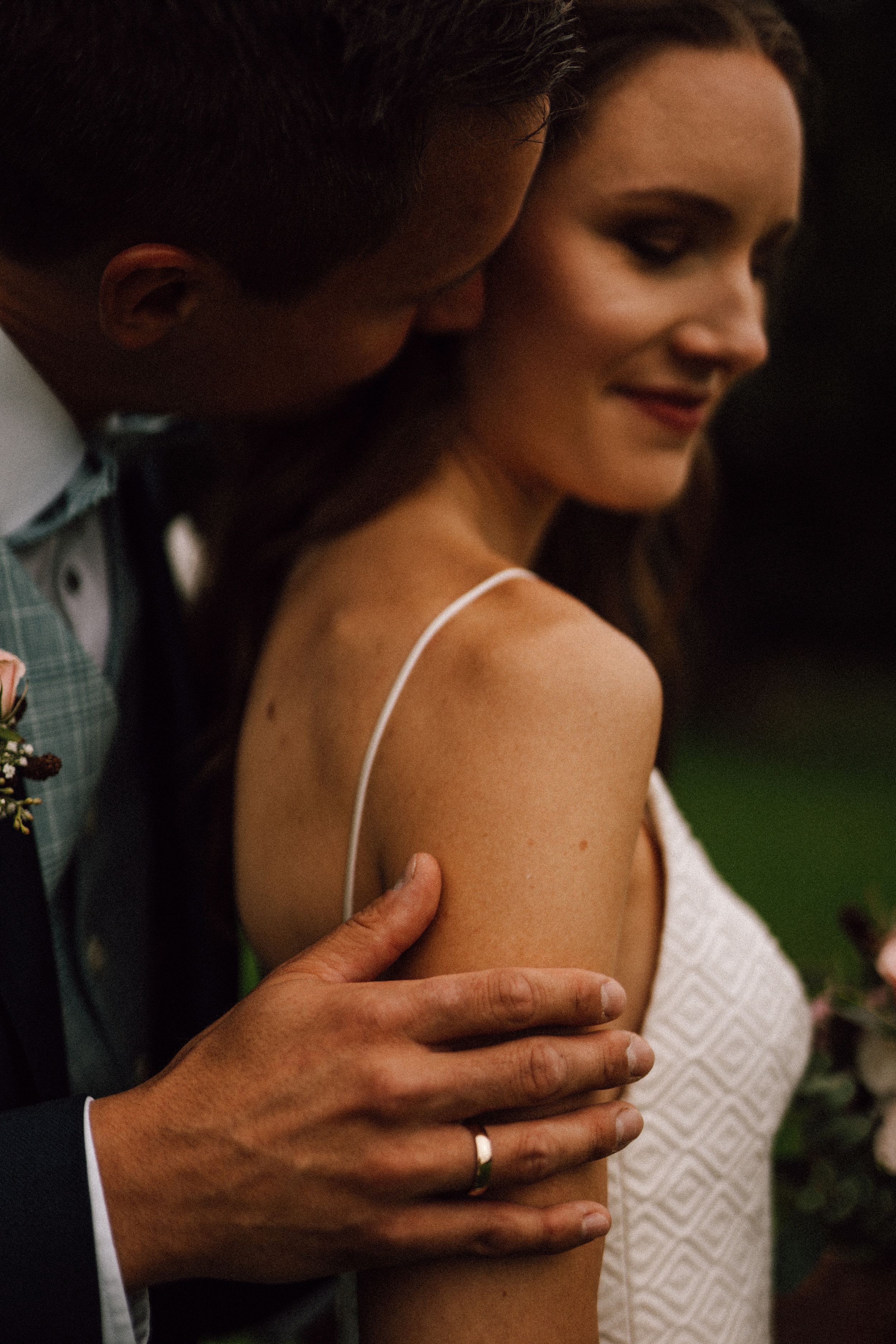 Close-up detail shot of hands and lace wedding dress in moody lighting.