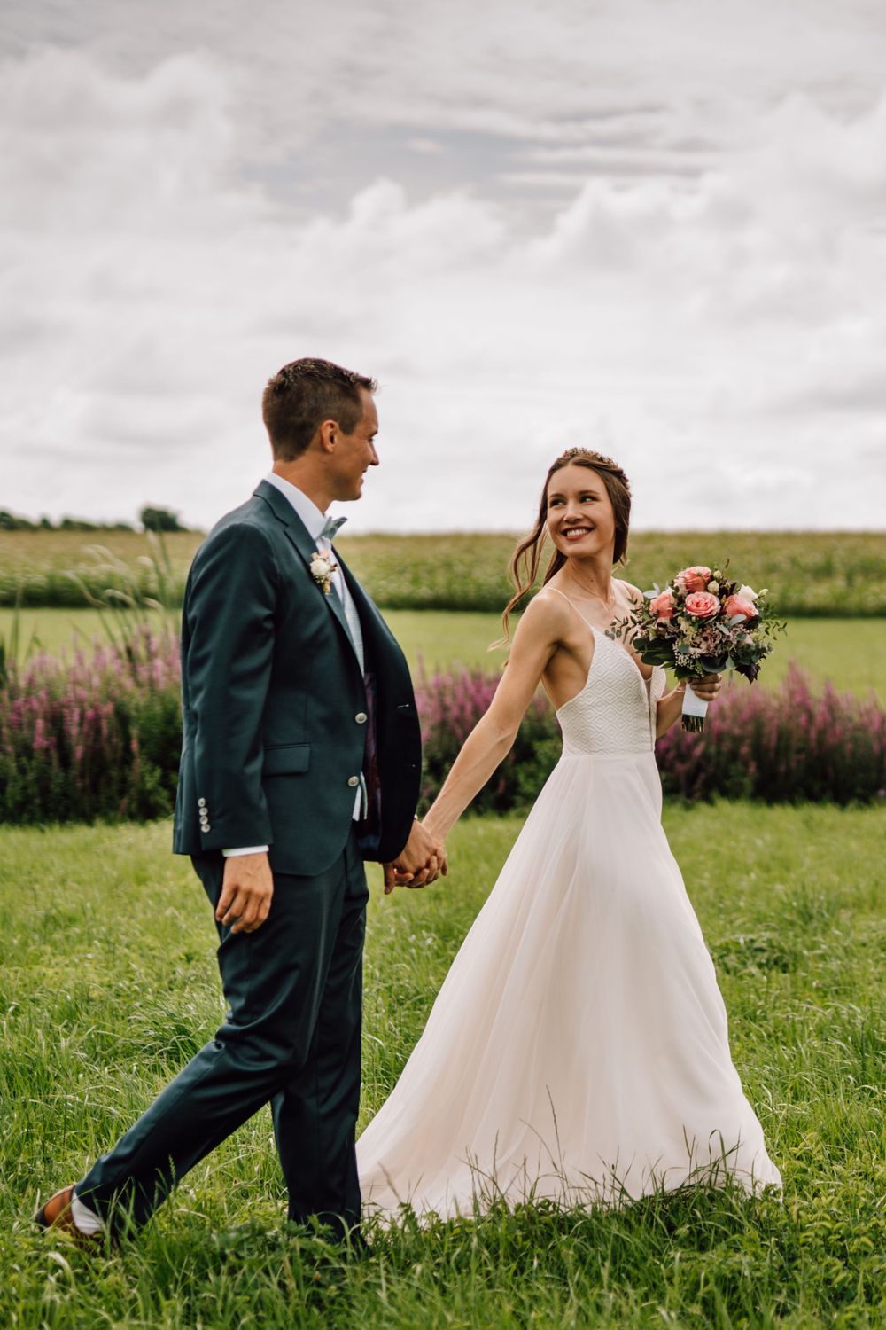 Joyful couple walking and laughing together in a green meadow with purple wildflowers.