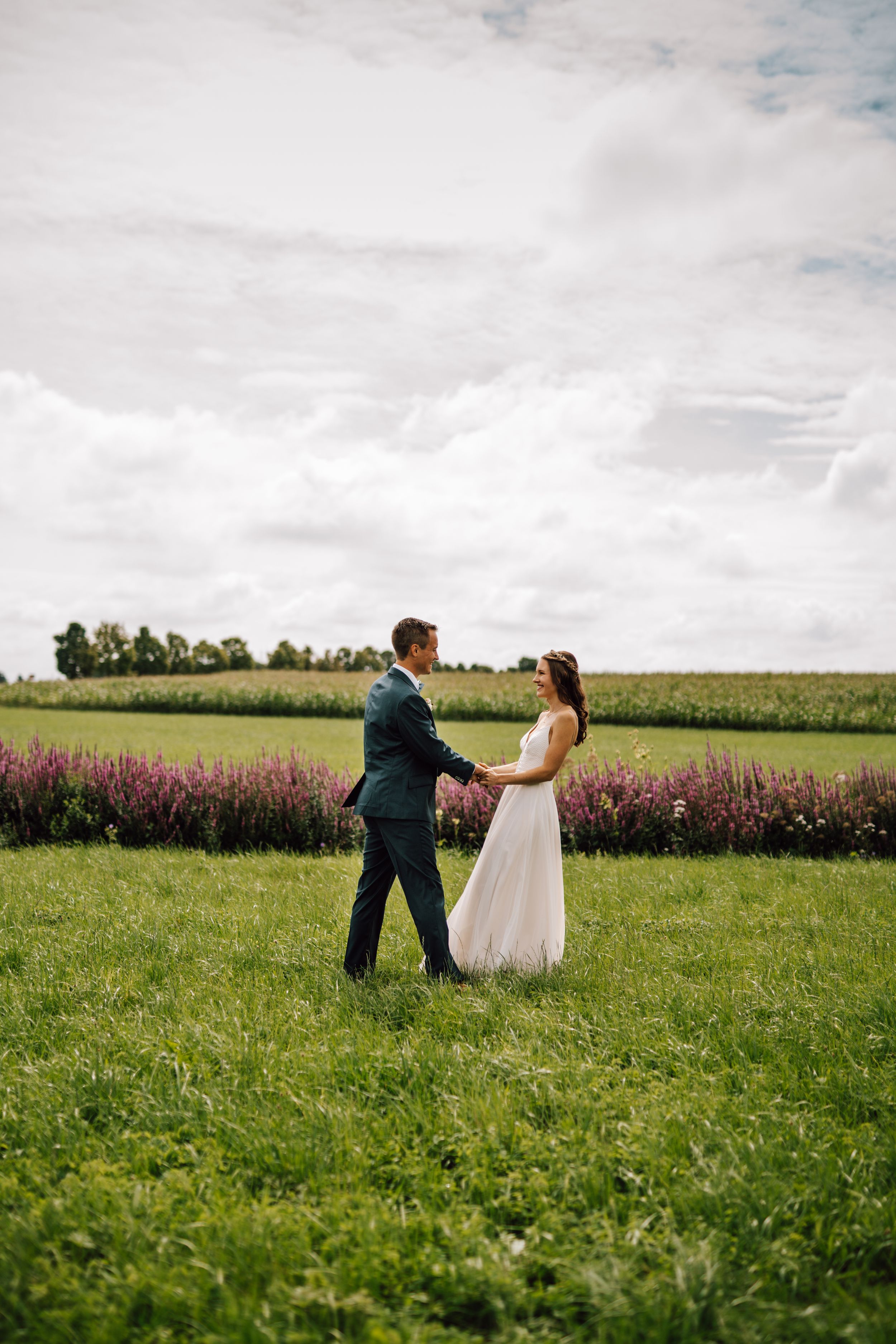 Playful wedding couple dancing and twirling in a sunny green field.