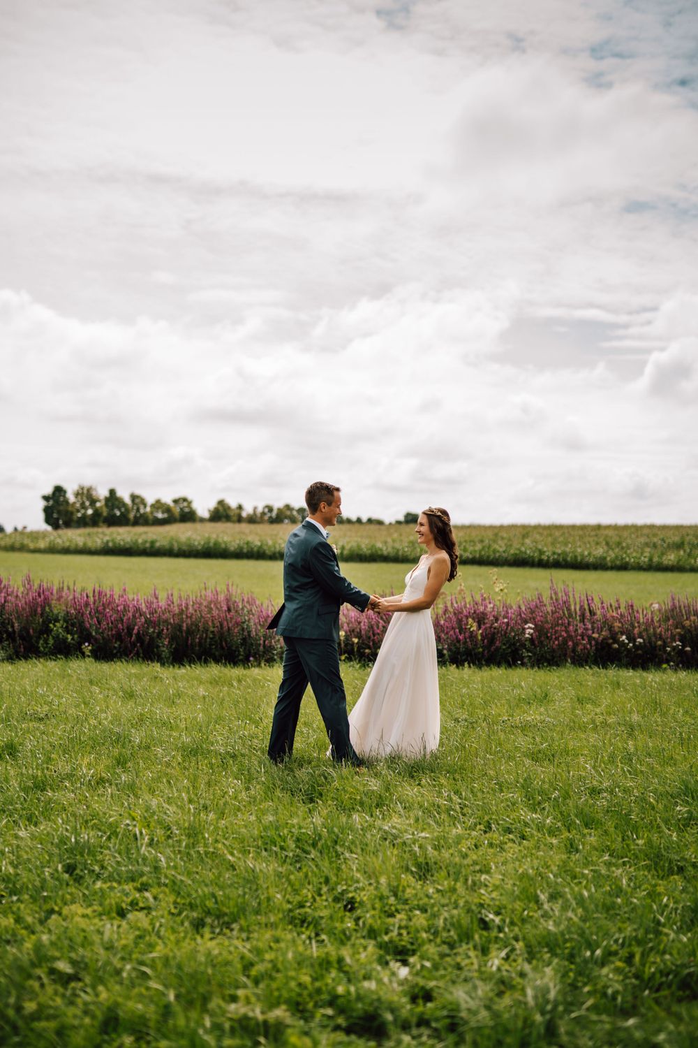 Playful wedding couple dancing and twirling in a sunny green field.