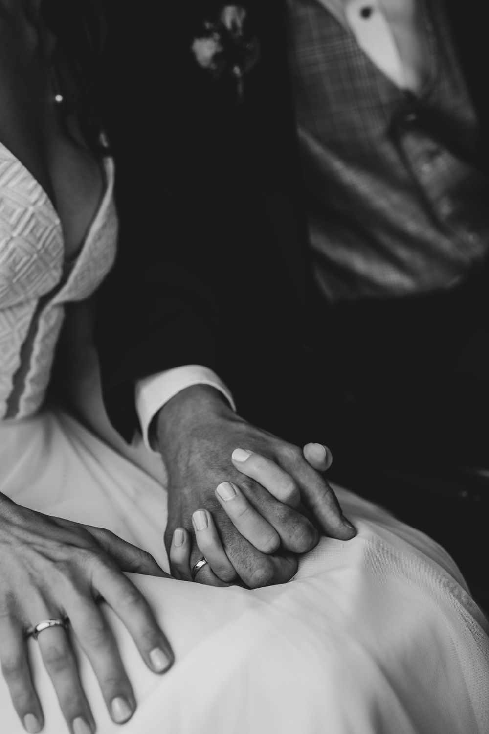 Black and white detail shot of hands resting on wedding dress fabric.