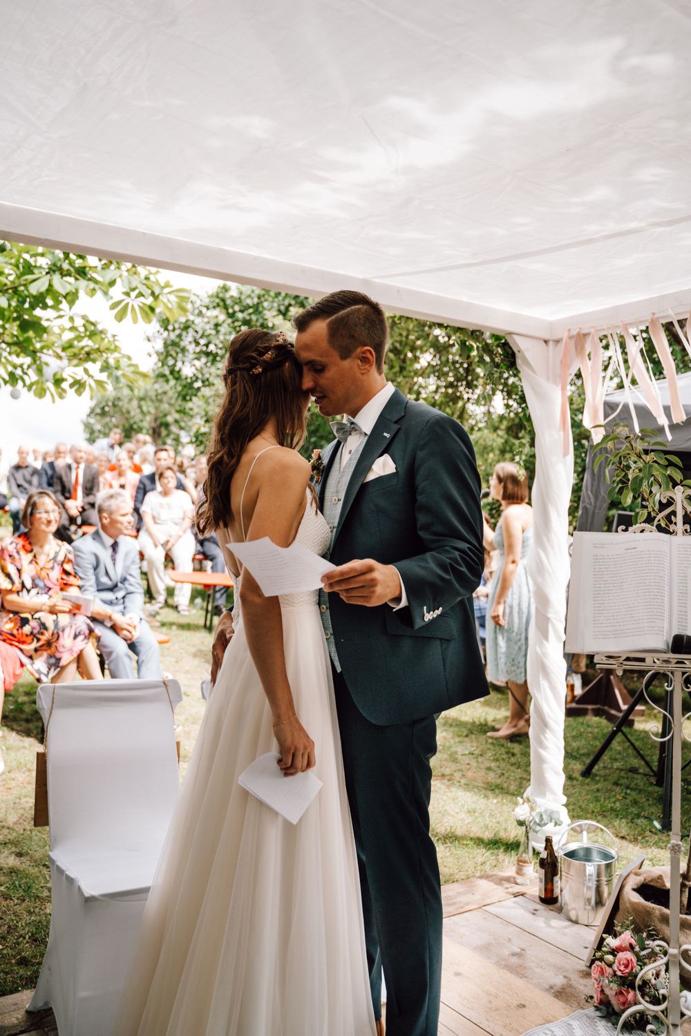 Wedding ceremony kiss under a white tent with guests watching.