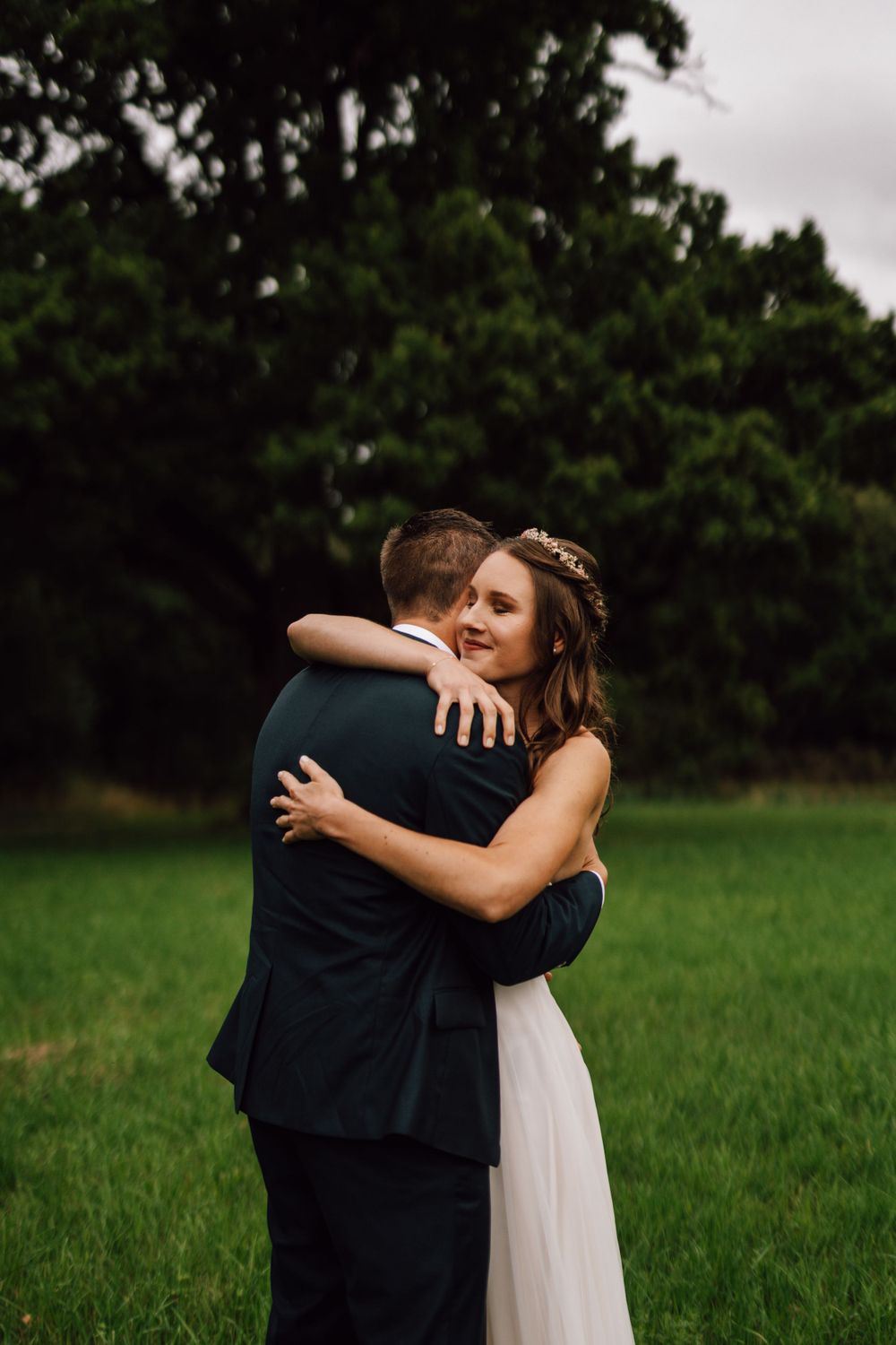 Tender embrace between newlyweds in a grassy field during golden hour.