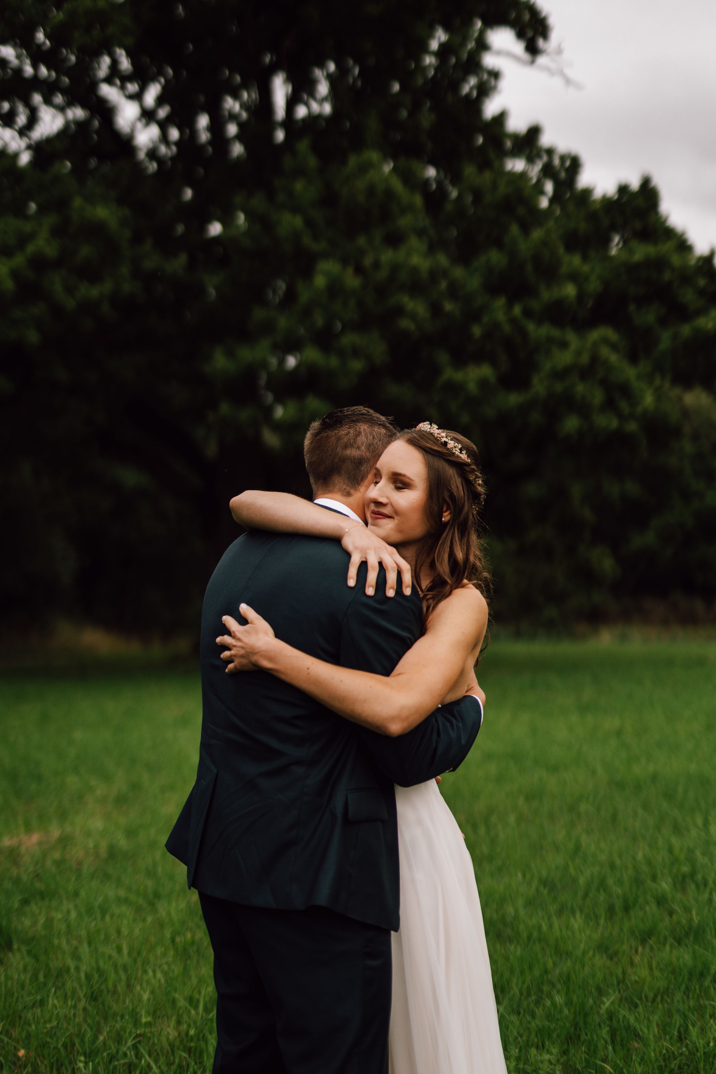 Tender embrace between newlyweds in a grassy field during golden hour.