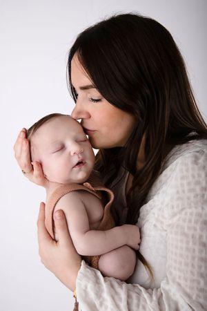 Intimate portrait of parent giving sleeping baby a gentle kiss against white background.