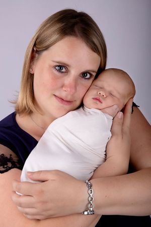 Mother in navy top holding sleeping swaddled newborn baby against purple backdrop.