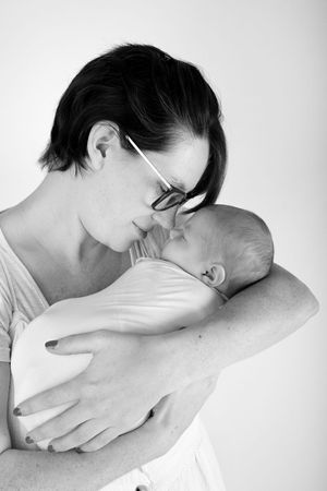 Intimate black and white portrait of mother in glasses embracing sleeping infant.