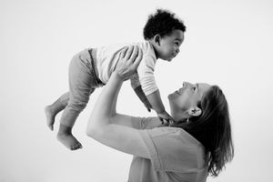 Black and white photo of mother lifting playful infant overhead.