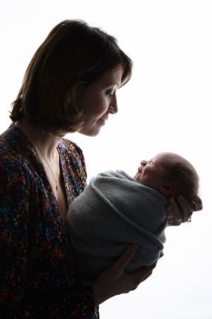 A silhouetted portrait of a woman in a floral dress holding a swaddled newborn baby against a white background.