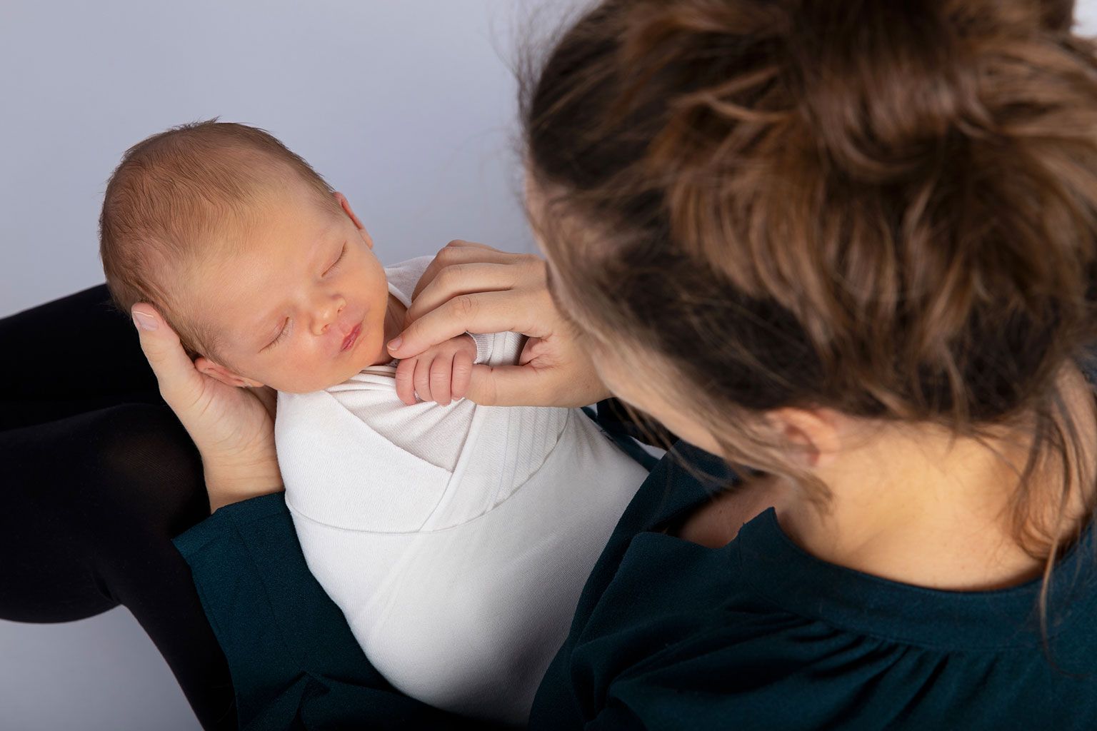 Intimate portrait of someone cradling a sleeping newborn baby dressed in white.