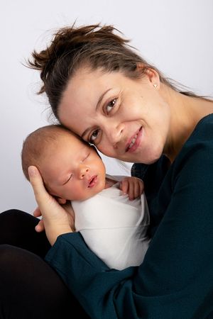 Close-up portrait of someone in teal sweater tenderly holding a sleeping newborn baby.