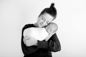 Black and white photo of someone in dark clothing embracing a sleeping newborn wrapped in white.
