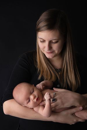 Low-key portrait of someone in black holding a peaceful sleeping baby against dark background.