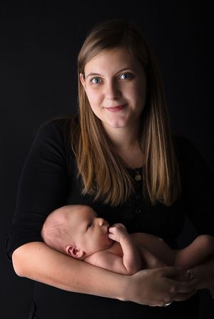 Artistic low-key portrait of someone holding a peaceful sleeping infant against black background.