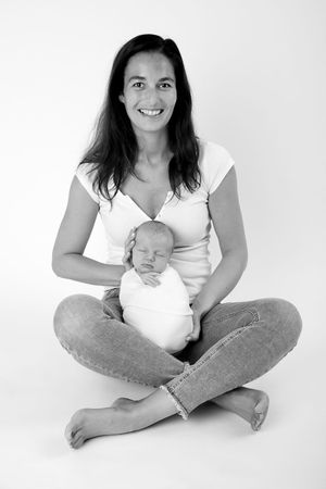 Black and white studio portrait of someone sitting cross-legged with sleeping newborn.