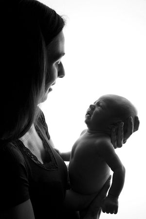 Silhouetted profile of someone holding and gazing at newborn baby against white background.