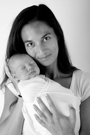 Black and white portrait of someone in white holding a sleeping newborn wrapped in white fabric.