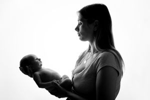 Silhouette profile of parent cradling newborn baby against white background.