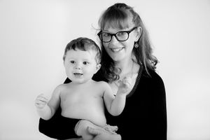 Parent in glasses shares joyful moment with smiling toddler against white backdrop.