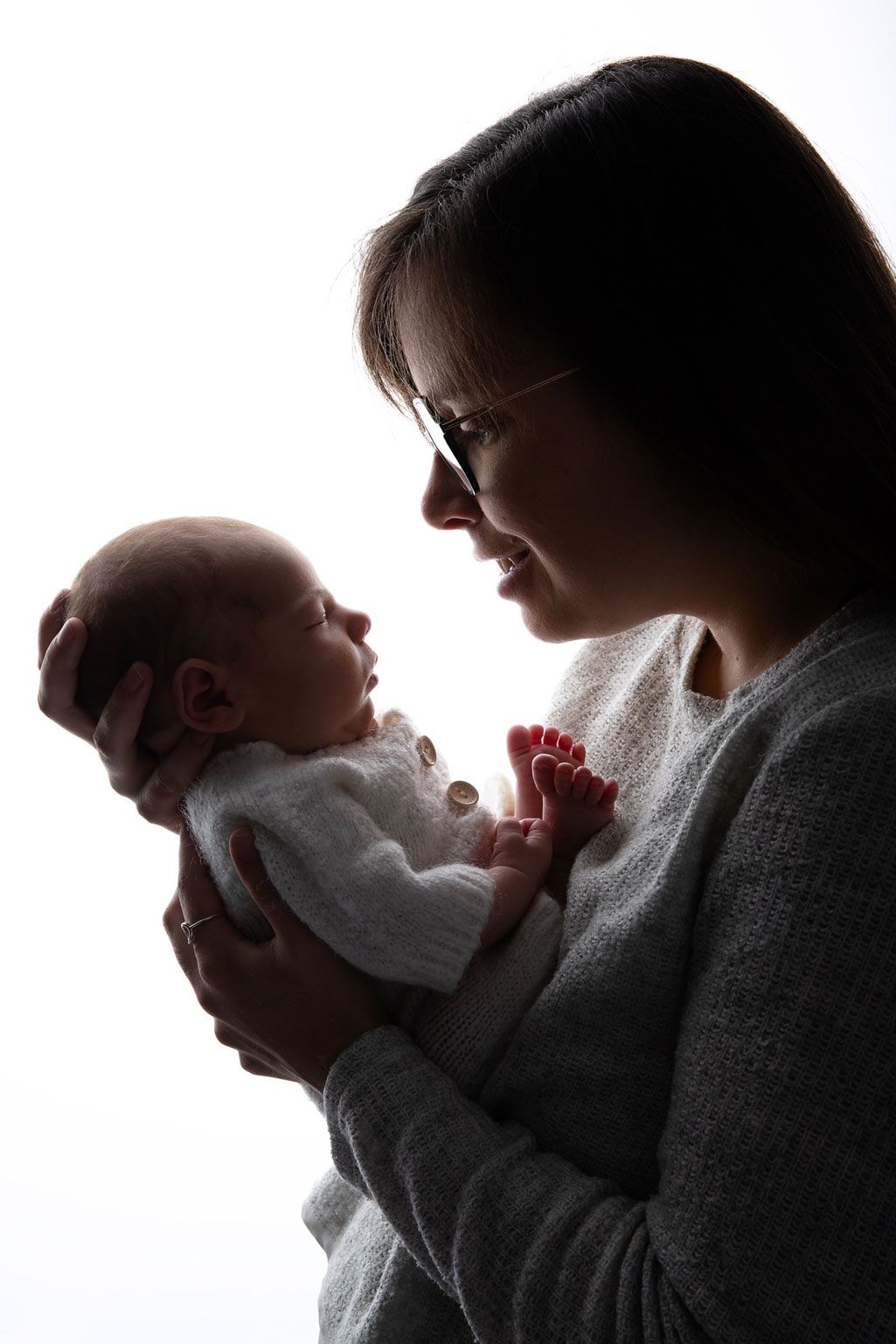 Silhouette of parent gazing at newborn baby while holding red flower.