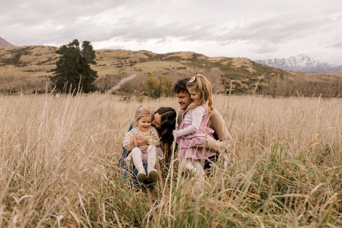 Family enjoys peaceful moment together in scenic mountain field with tall grass.