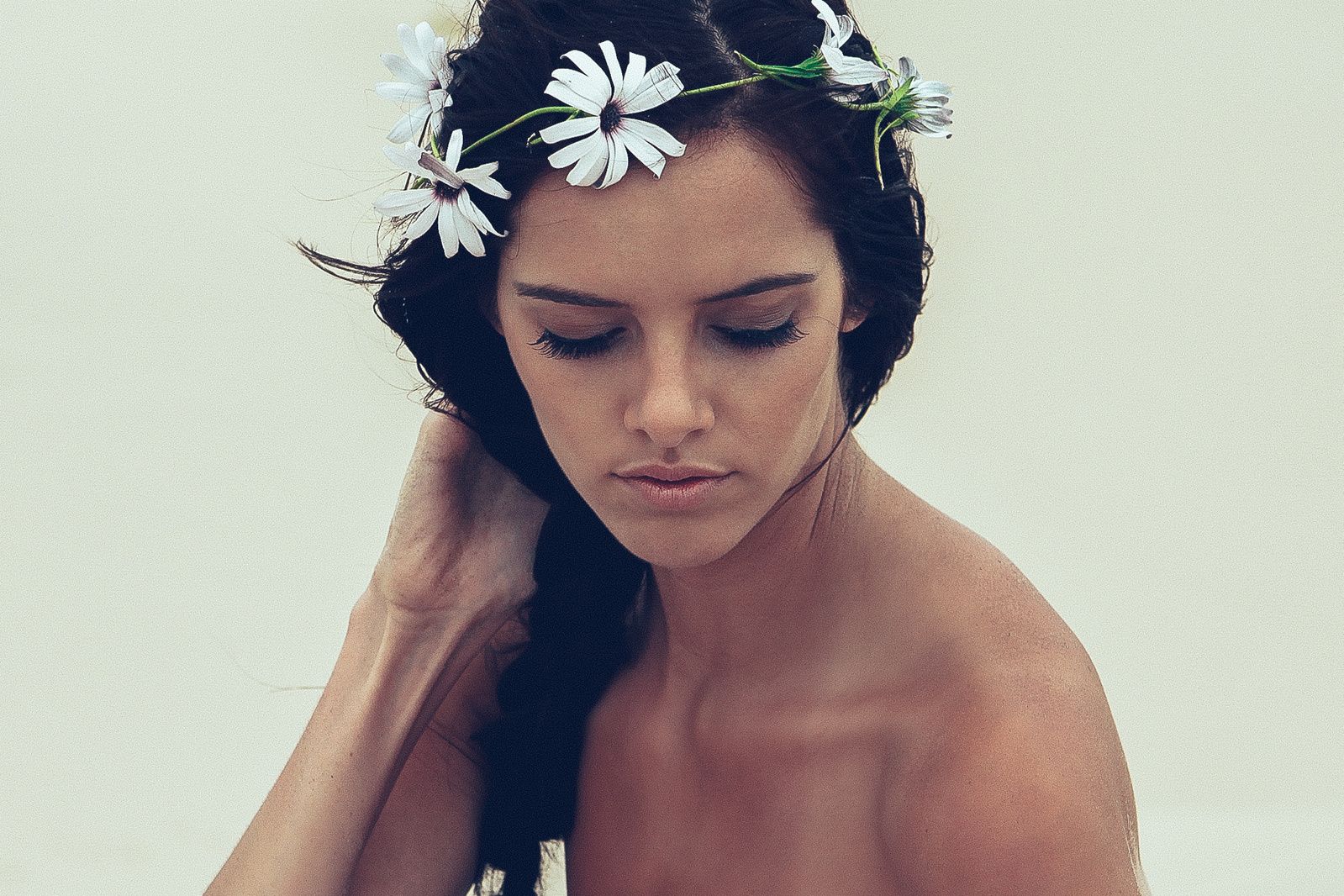 Model wearing floral crown poses against light background in artistic portrait.