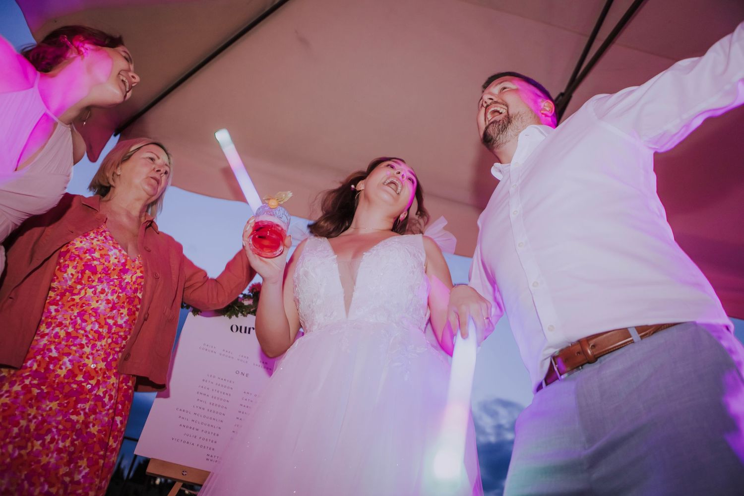 Wedding reception party guests dancing under pink lighting at an outdoor celebration.