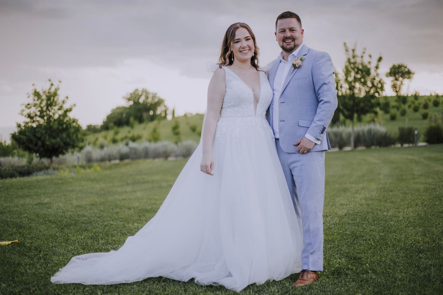 Bride and groom in formal wedding attire posing for portraits on a lawn.