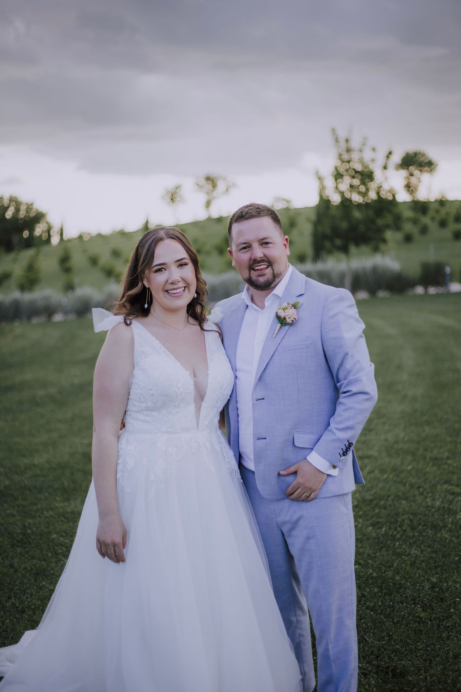 Newlyweds posing together on a grassy hillside at their wedding.
