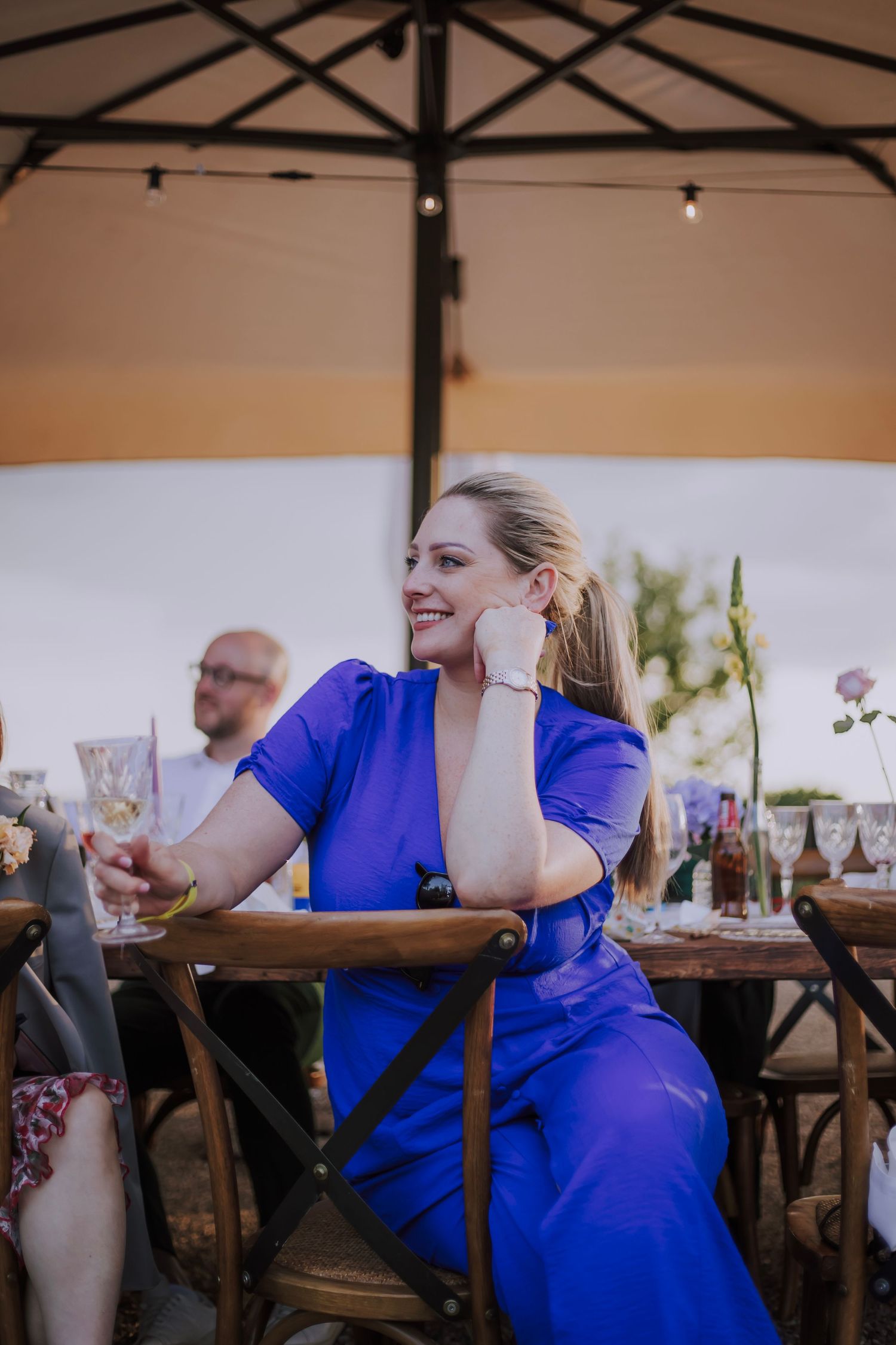 Guest in blue dress enjoying conversation at outdoor wedding reception.
