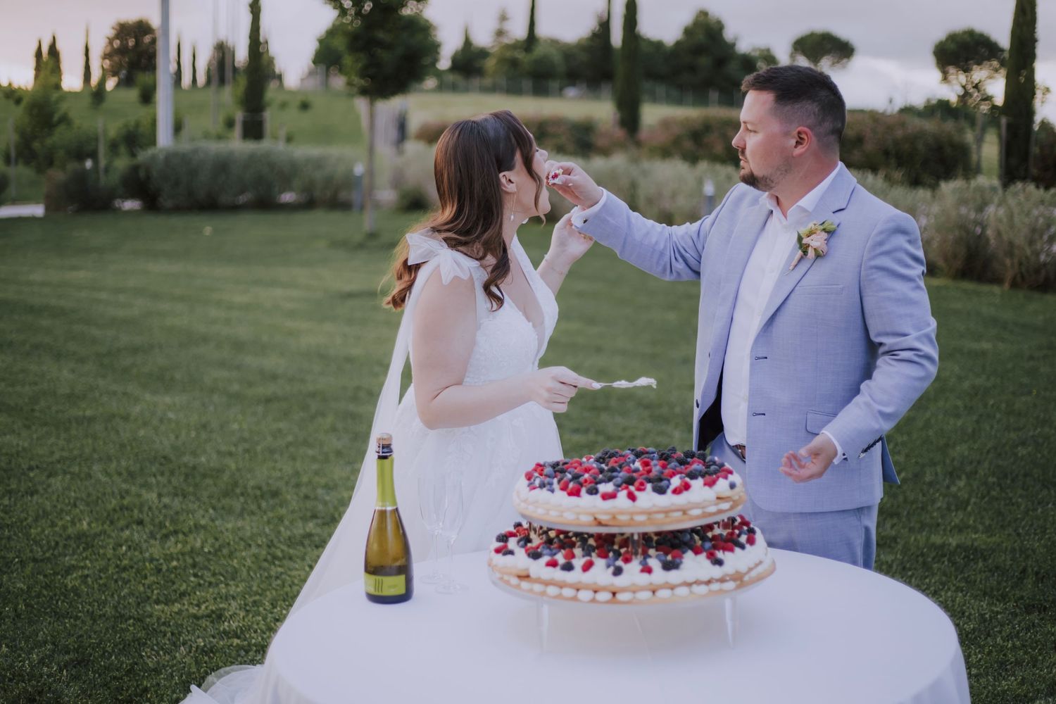 Couple playfully feeds each other wedding cake during their outdoor garden reception.