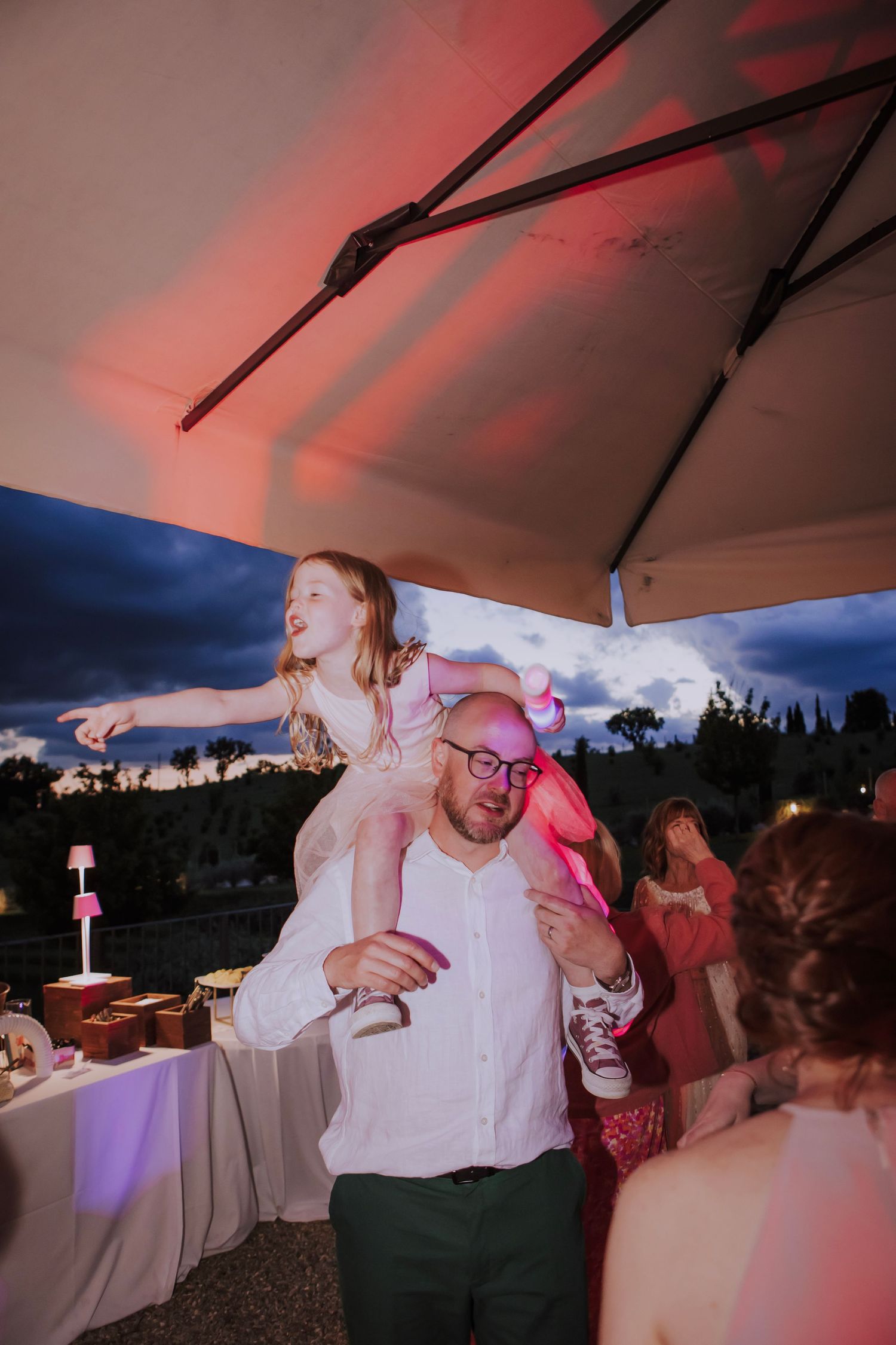 Dancing and celebration under a red-lit tent at an outdoor wedding reception.