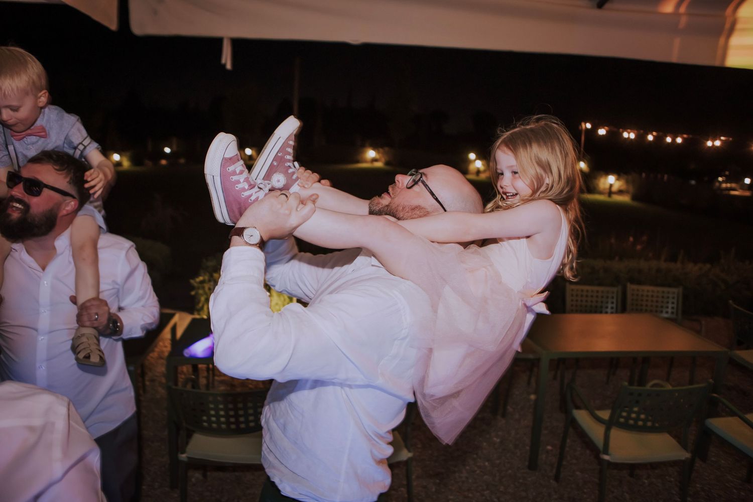 Playful lift during wedding reception dance party under outdoor tent lighting.