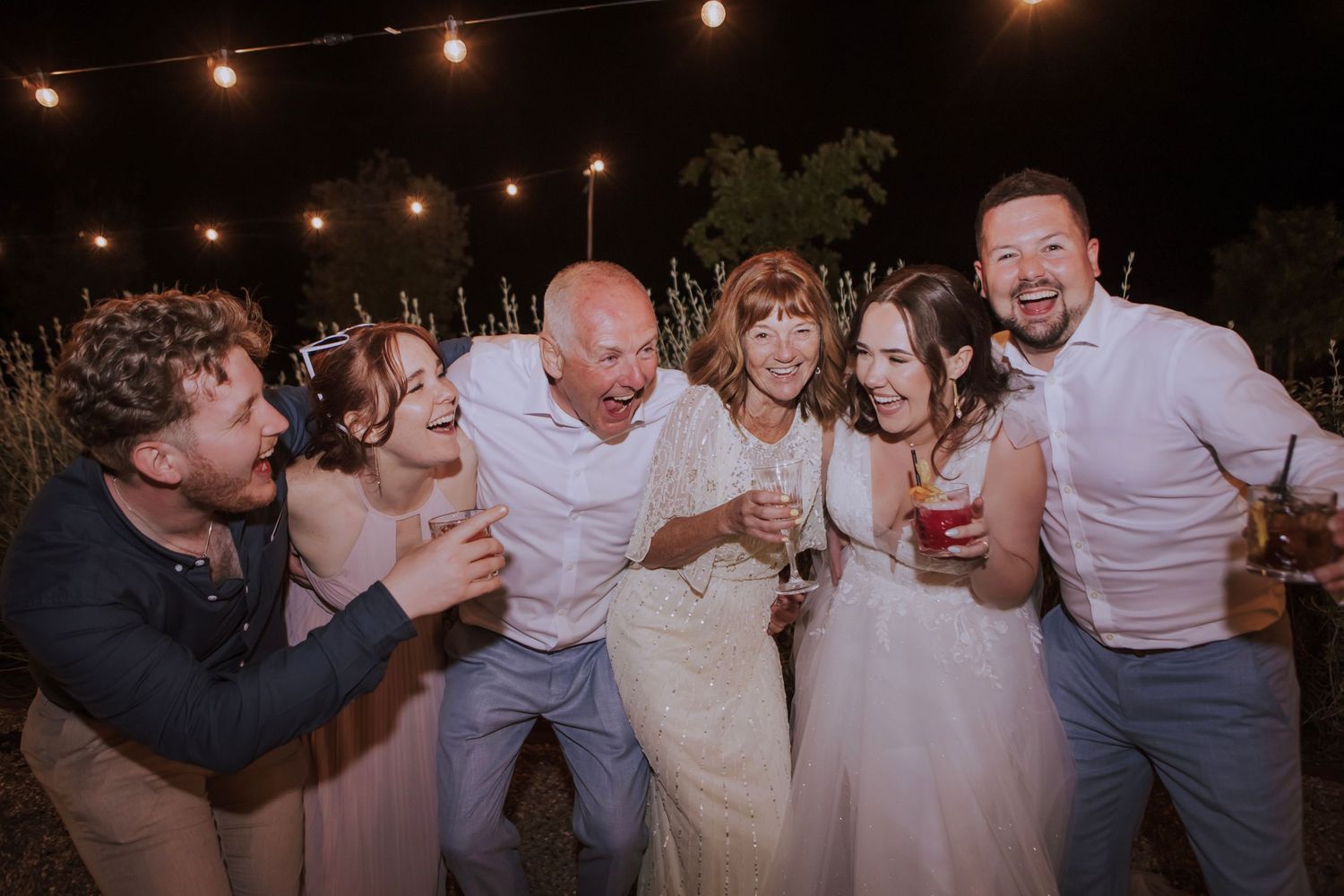Joyful group celebration moment captured under string lights at outdoor wedding reception.