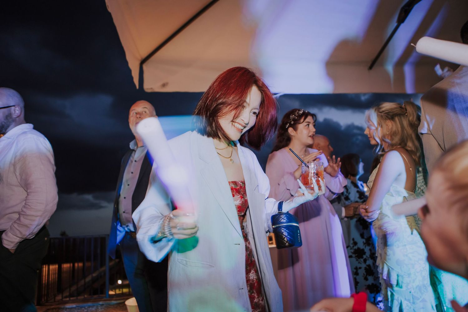 Guests enjoying drinks and mingling at a festive evening wedding reception under a tent.