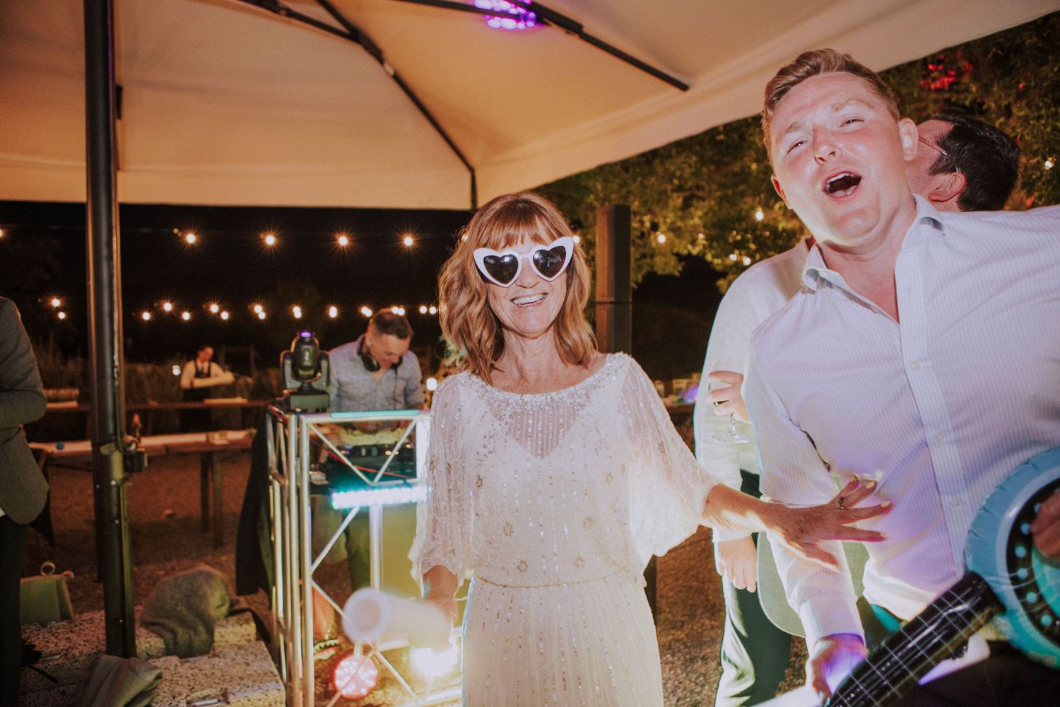 Wedding celebration under tent with string lights as guests dance and enjoy the festivities.