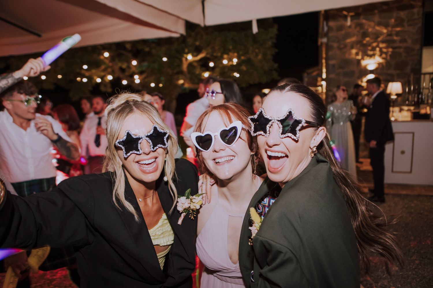 Party guests wearing matching star-shaped sunglasses pose together at evening reception.