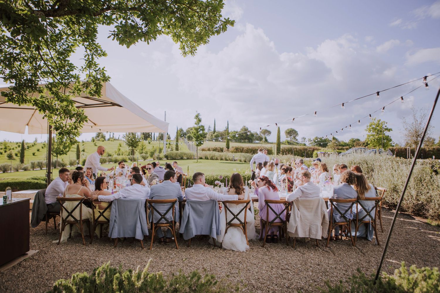 Long dining table set for outdoor wedding reception under string lights.