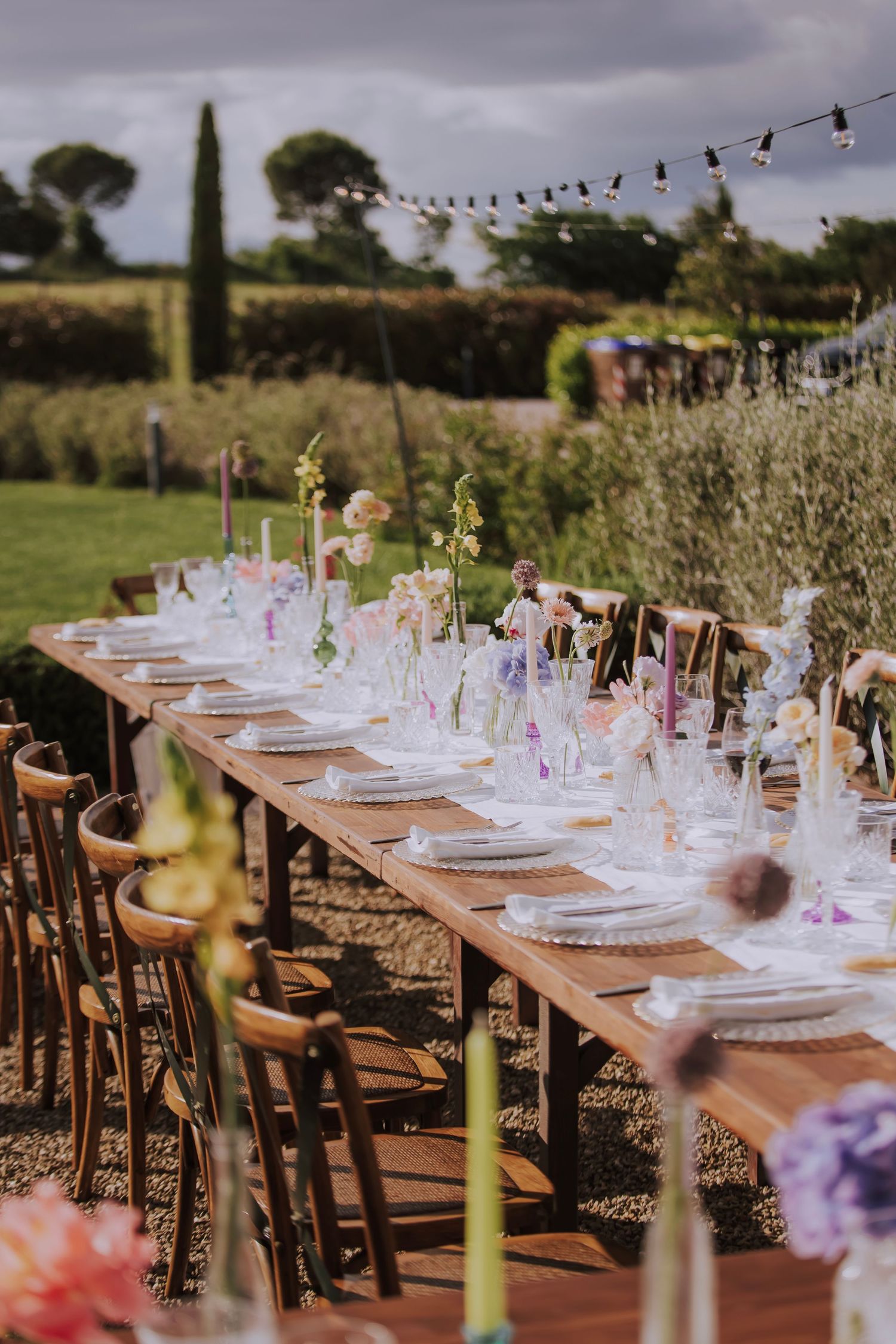 Elegant outdoor wedding table setting with string lights and purple floral arrangements.
