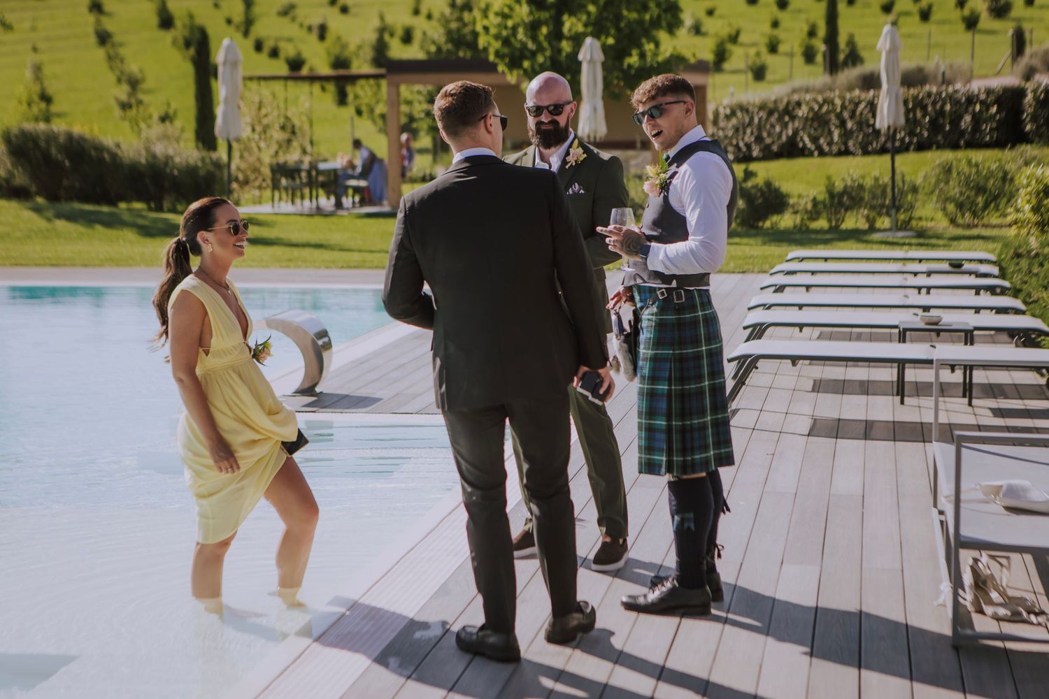 Small group gathering on wooden deck with person wearing traditional Scottish kilt.