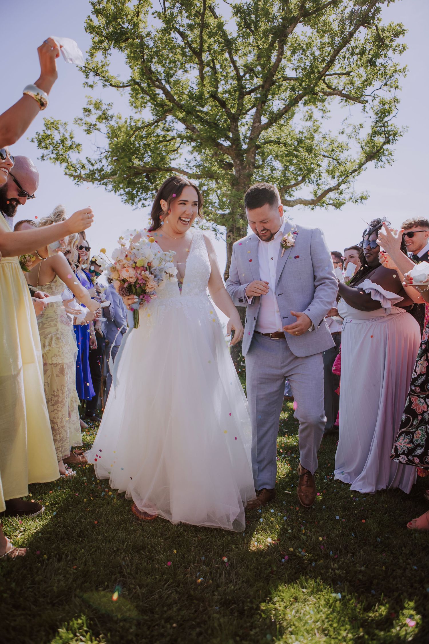 A couple walks through a crowd of guests during their outdoor wedding celebration.
