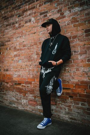 Person in black hoodie and blue Converse leaning against urban brick wall.
